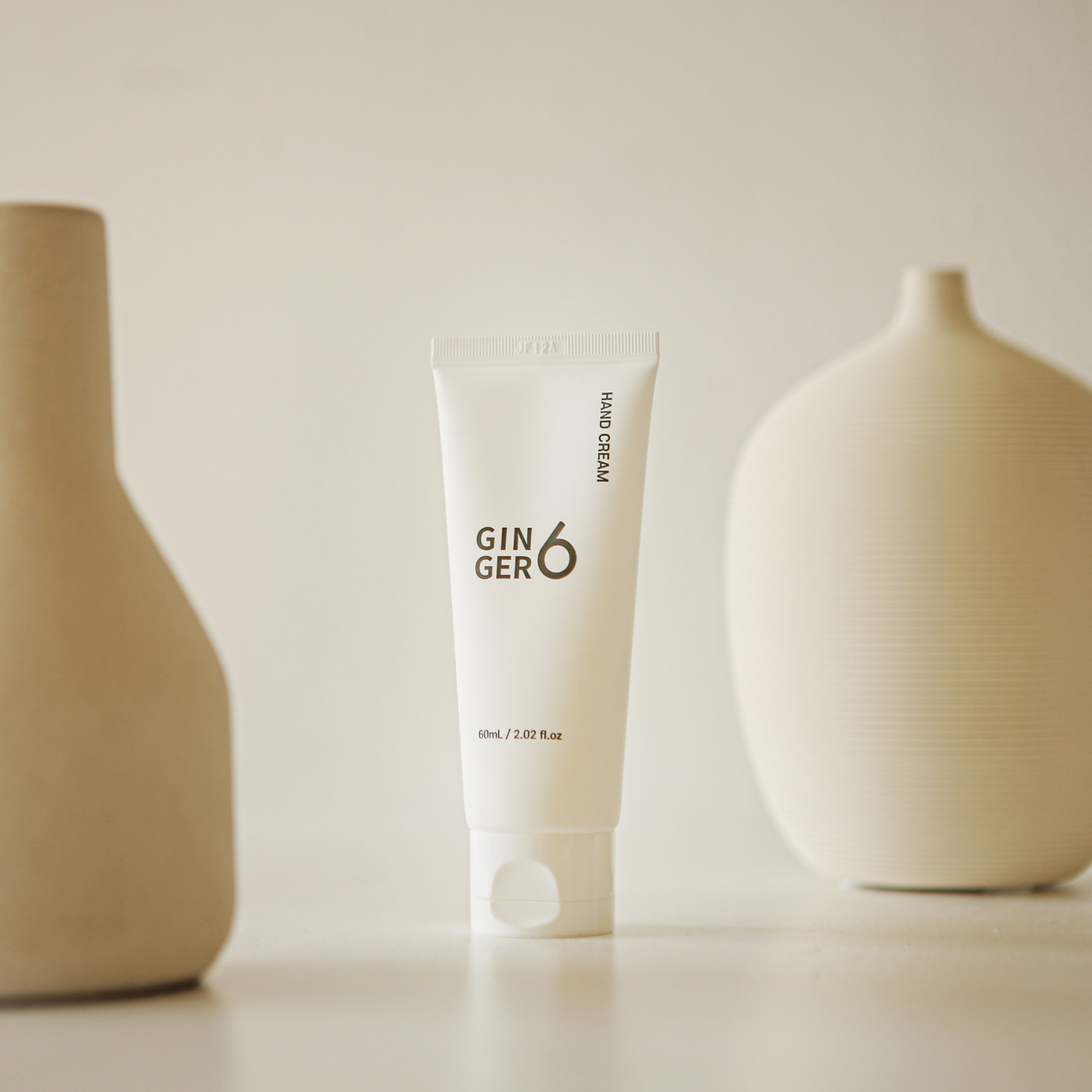 Ginger6 Hand Cream elegantly placed between modern beige ceramic vases on a clean surface